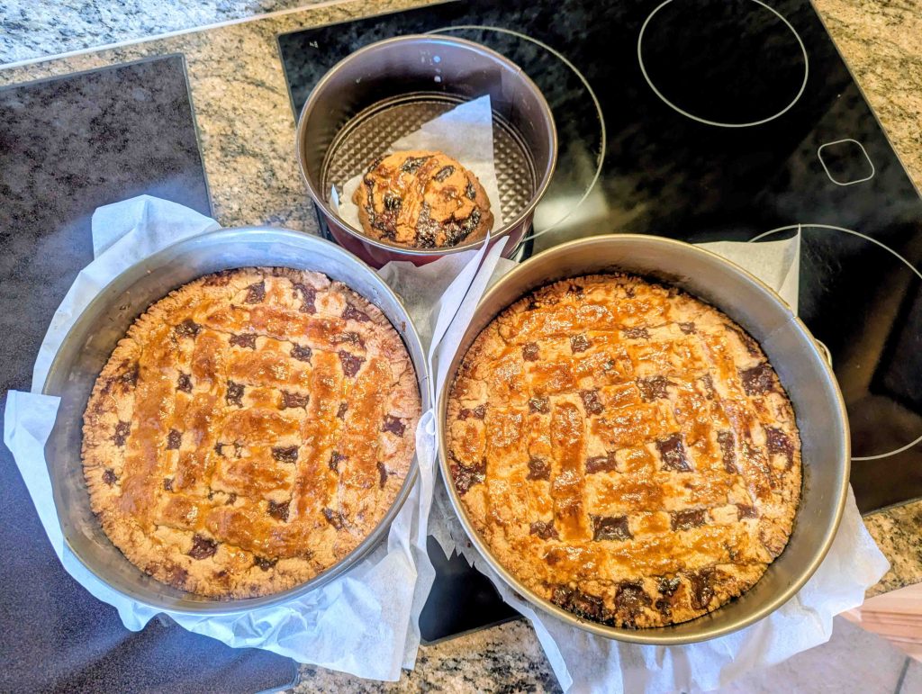Three freshly baked golden brown Linzertortes with lattice crust in springform pans on black cooktop
