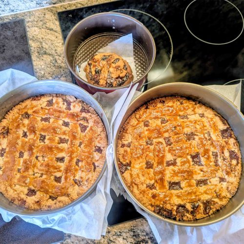Three freshly baked golden brown Linzertortes with lattice crust in springform pans on black cooktop