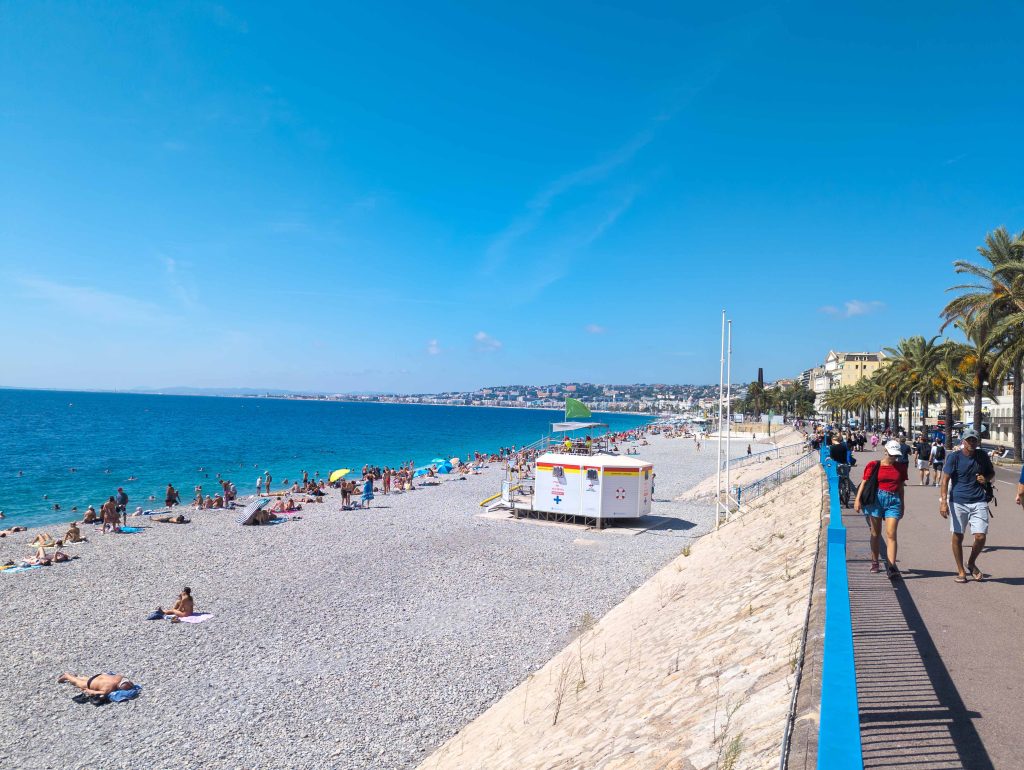 Pebble beach along the Promenade des Anglais in Nice with sunbathers near a lifeguard station and azure Mediterranean water