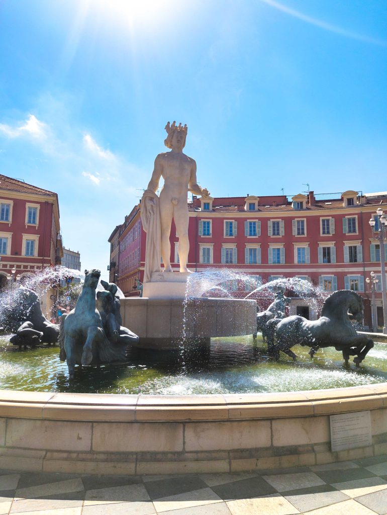 Fontaine du Soleil on Place Massena in Nice featuring the statue of Apollo surrounded by leaping bronze horses and red neoclassical facades