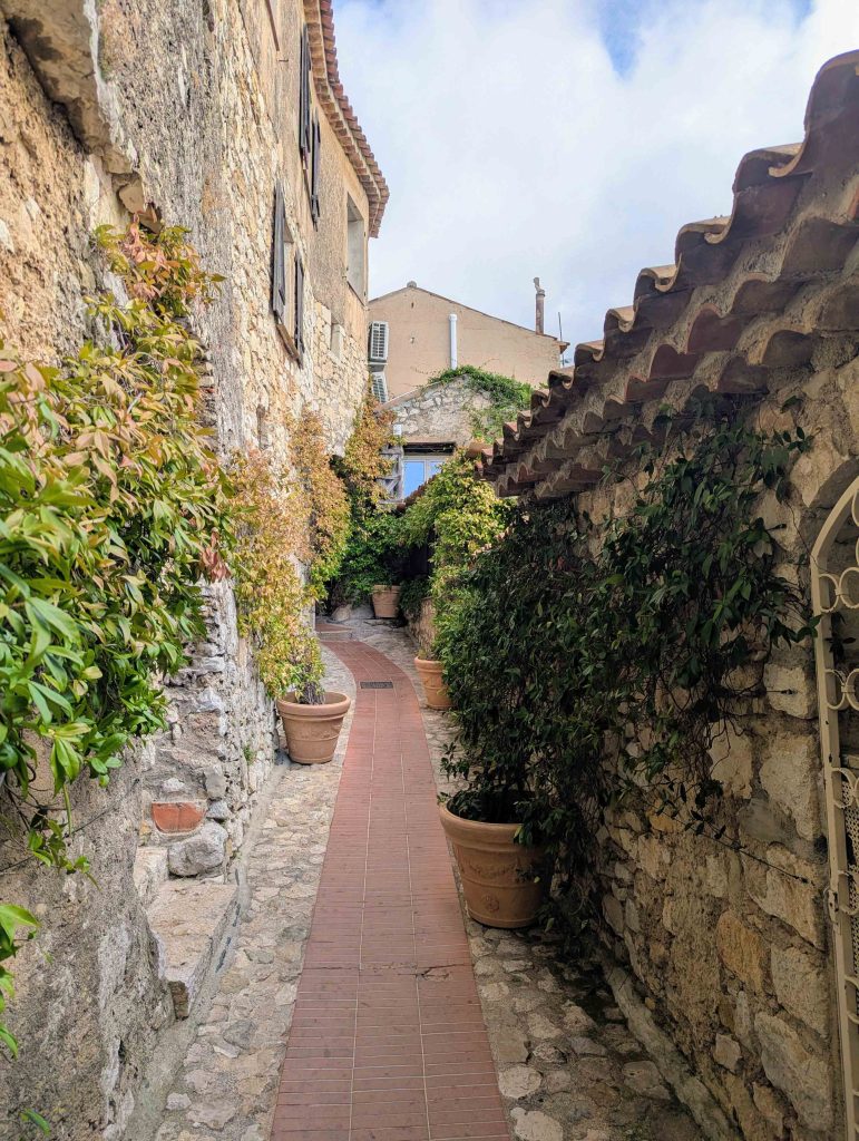 Narrow cobblestone pedestrian alleyway in medieval Eze with stone buildings and terracotta potted plants