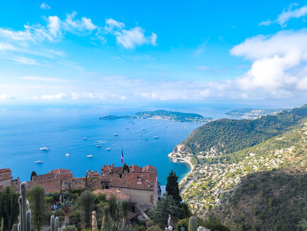 Panoramic view from the summit of Jardin Exotique over medieval Eze rooftops and the French tricolor flag above the Mediterranean Sea