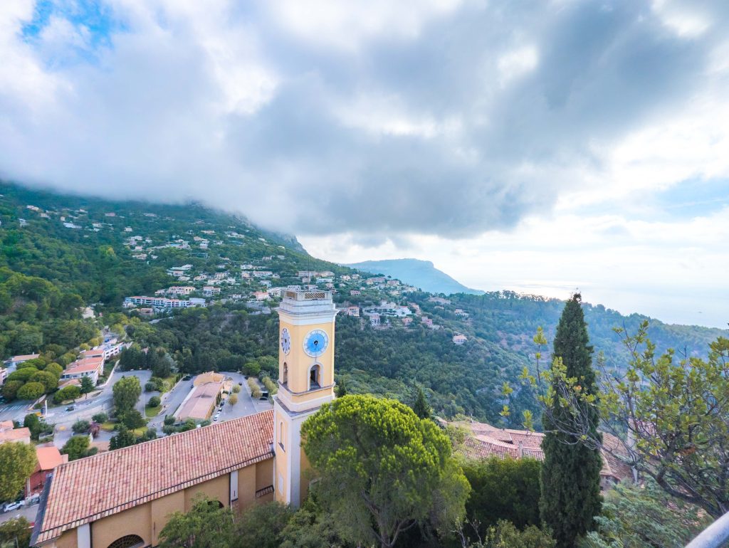 Neoclassical clock tower of the church in Eze framed by exotic cacti and surrounding mountain ridges