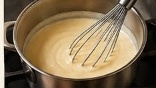 Wire whisk stirring melted cheese into warm bechamel sauce in saucepan