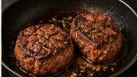 Two thick beef tenderloin steaks searing in foaming butter in heavy skillet