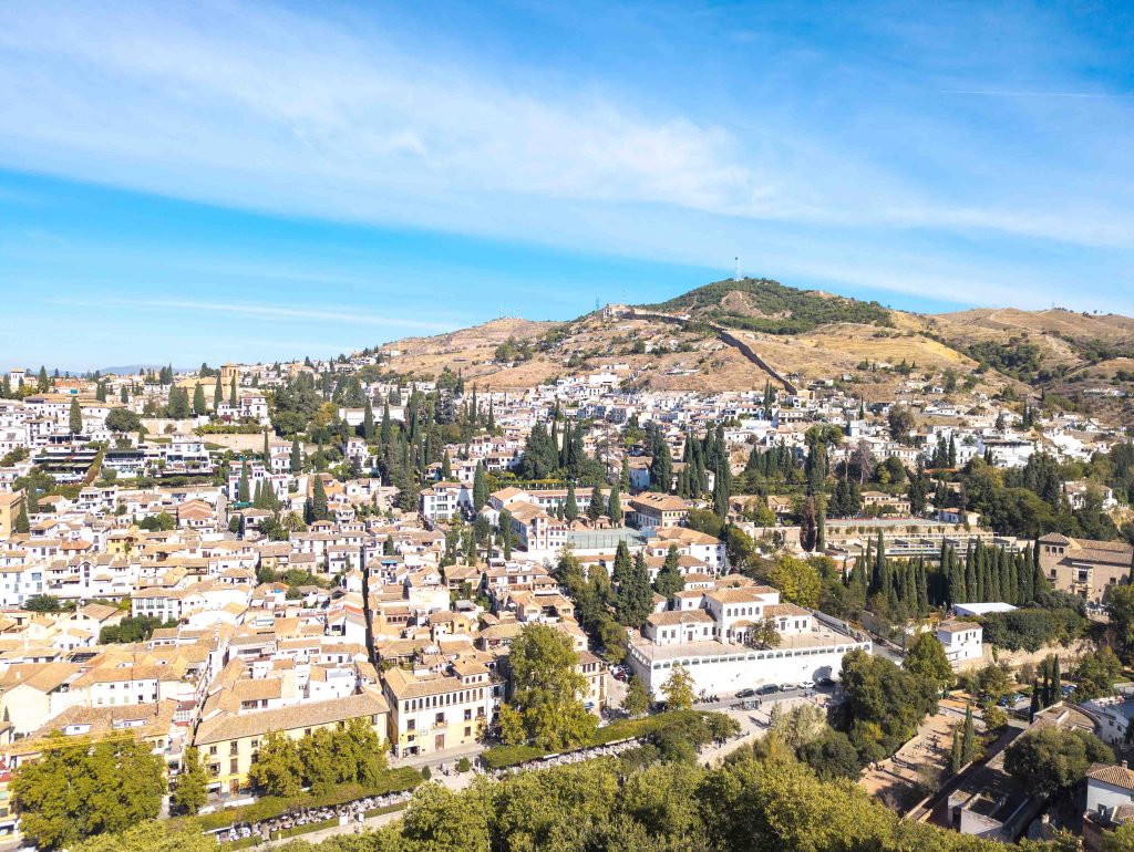 Sunlit panoramic view from the Alhambra looking across the whitewashed houses terracotta roofs and cypress trees of the Albaicin hillside