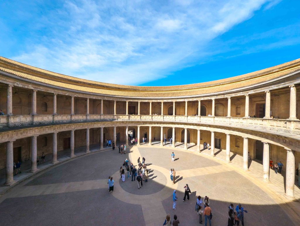 Grand circular Renaissance courtyard ringed by two tiers of Doric and Ionic stone colonnades inside the Palace of Charles V at the Alhambra