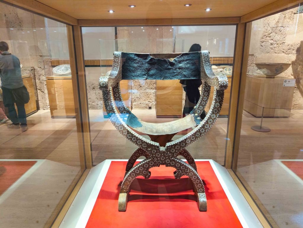 Fifteenth century Nasrid wooden folding chair inlaid with geometric bone marquetry and a tooled leather backrest in the Alhambra Museum