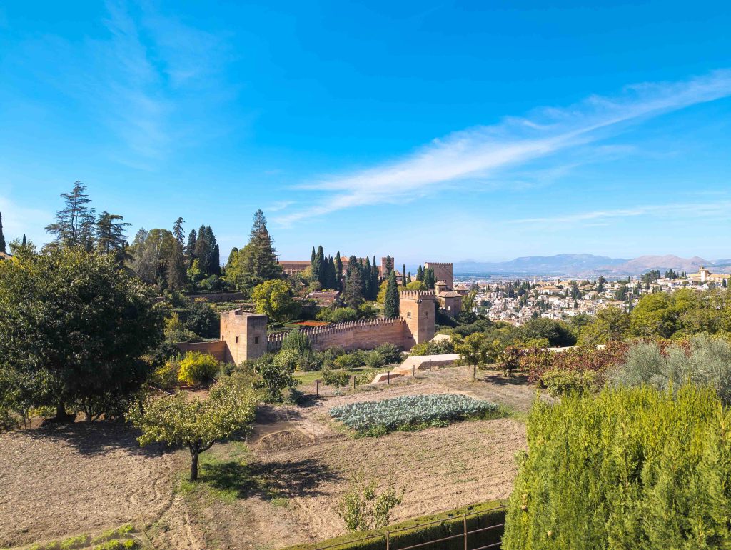 View across terraced orchards from the Generalife toward the red fortified walls and watchtowers of the Alhambra above Granada