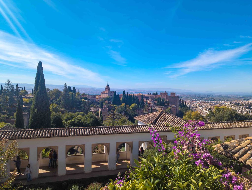 Whitewashed arched walkway and purple bougainvillea blossoms in the Generalife gardens overlooking the red towers of the Alhambra