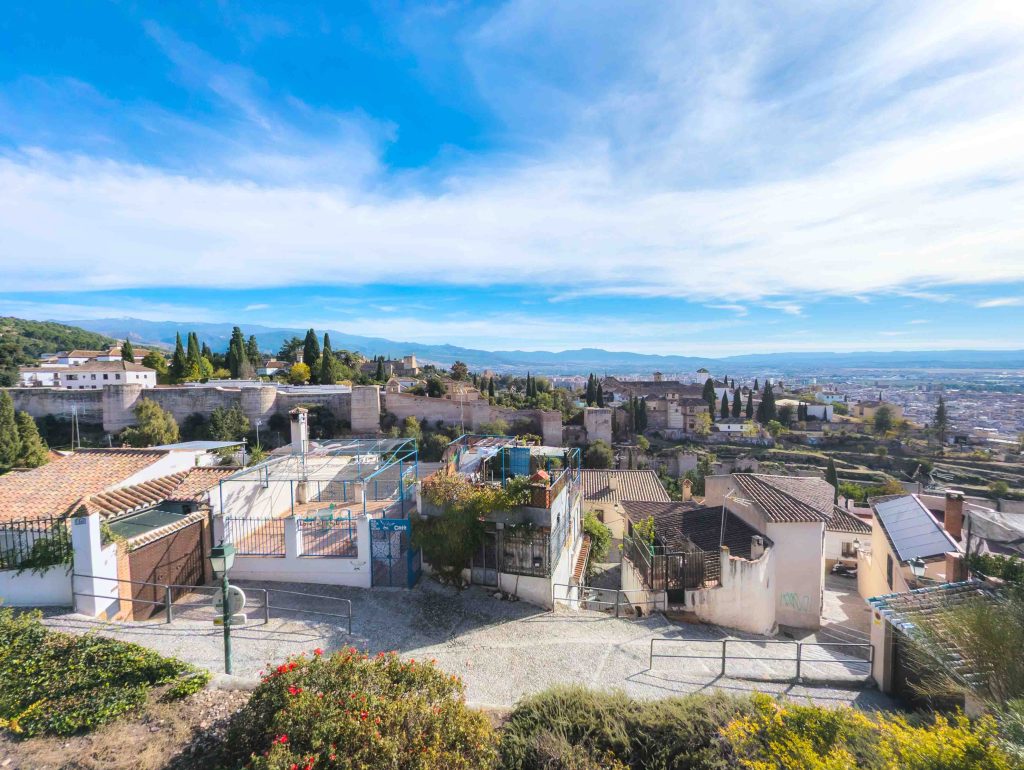 Elevated viewpoint from the Albaicin neighborhood looking over terracotta rooftops toward the fortified walls of the Alhambra on the Sabika hill