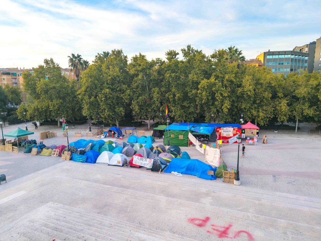 Cluster of colorful protest tents and banners pitched on a wide stone plaza near the Congress Center in Granada