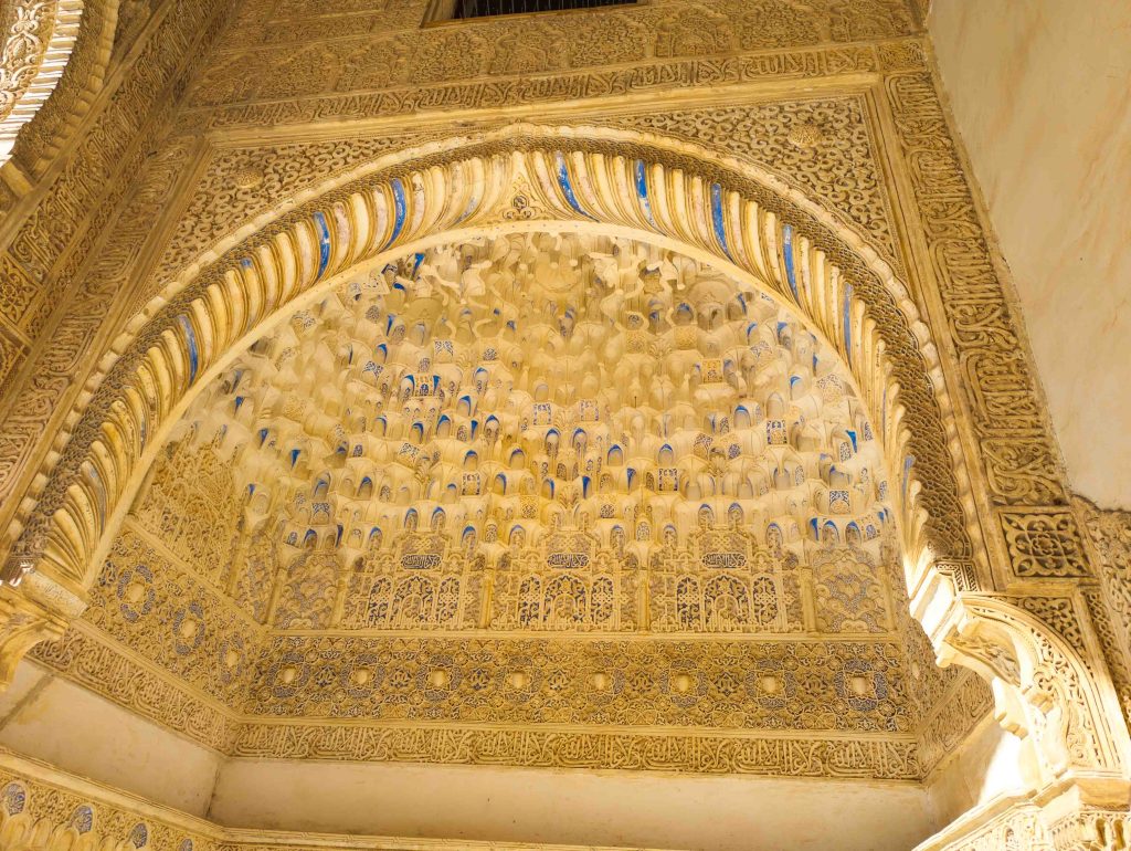 Intricate carved stucco archway and honeycombed muqarnas vaulting with blue pigment details inside the Nasrid Palaces at the Alhambra