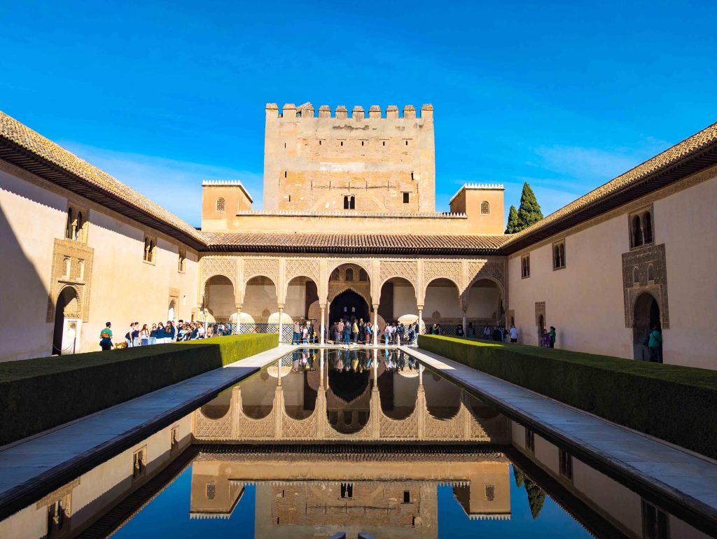 Symmetrical reflection of the Comares Tower and its seven arched portico in the still emerald water of the Court of the Myrtles at the Alhambra