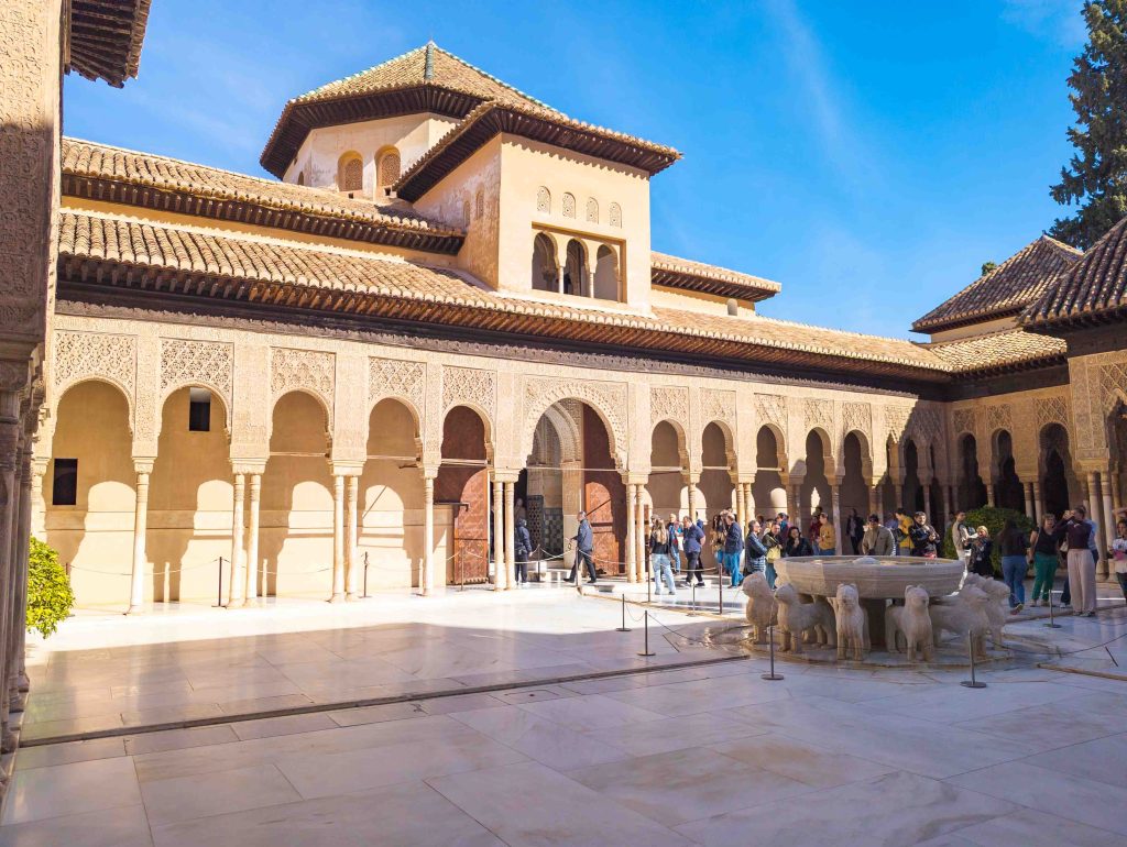 Wide view of the Court of the Lions showcasing slender white marble columns ornate stucco pavilions and the central lion fountain
