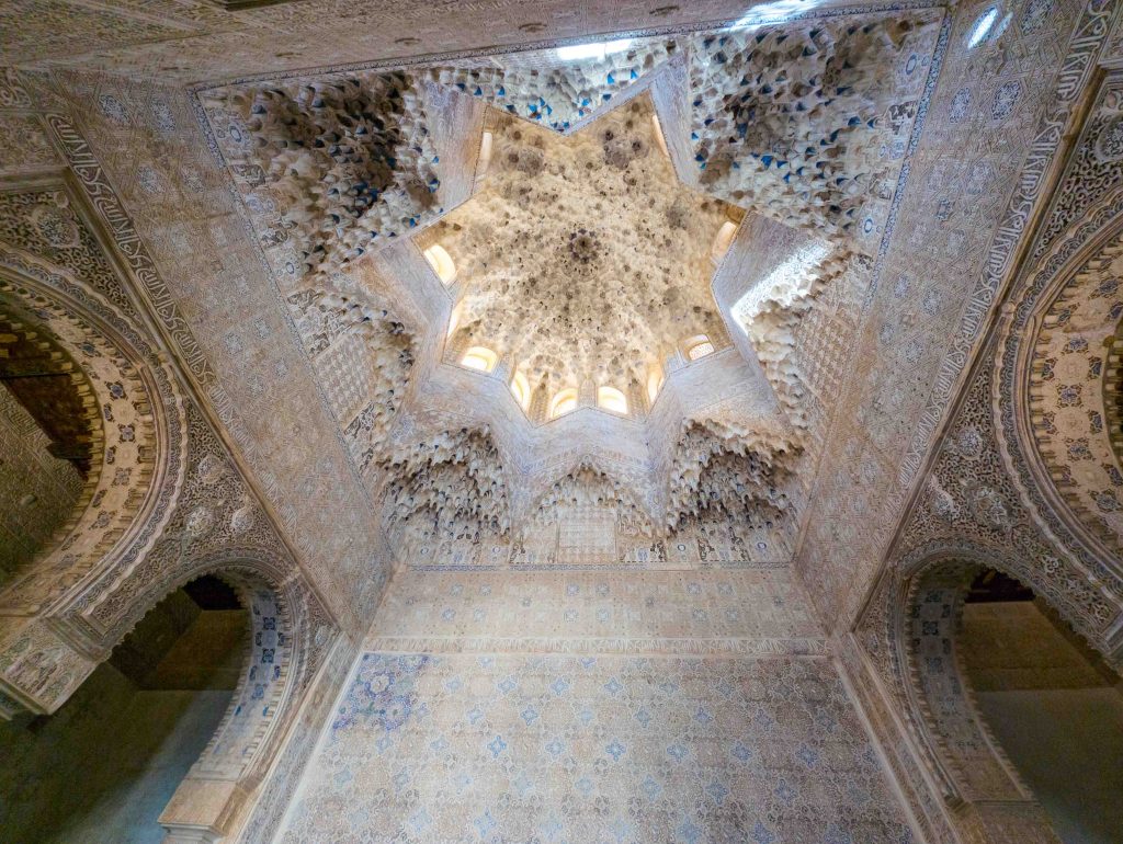 Upward view of the intricate octagonal muqarnas honeycomb ceiling illuminated by clerestory windows in the Hall of the Two Sisters at the Alhambra